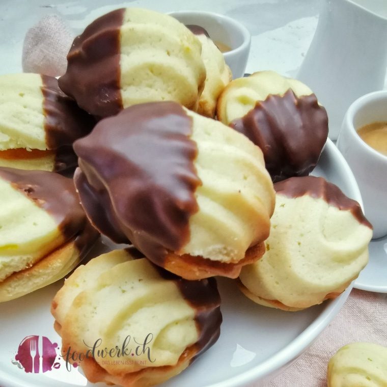 Züri Nüssli Plätzchen, Spritzgebäack mit Marmelade und Schokoladenglasur auf weissem Teller mit Kaffee im Hintergrund