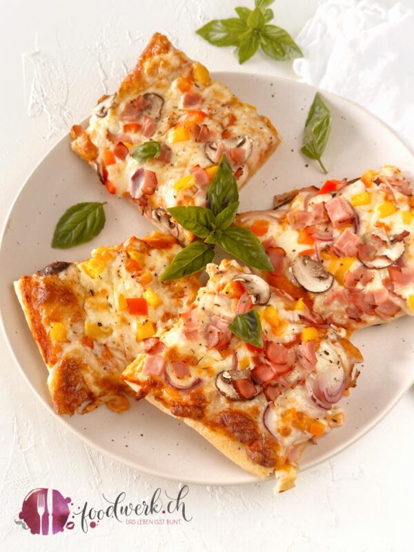 4 Stücke der Blechpizza auf einem Teller angerichtet mit Basilikum