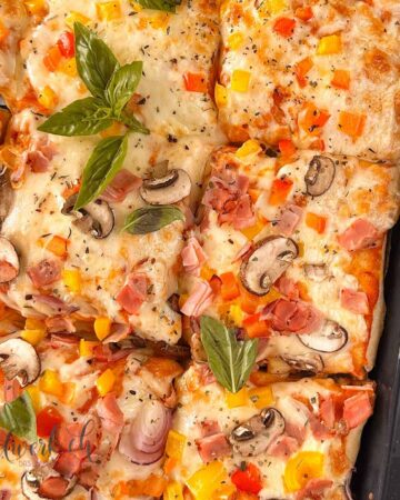 Fertig gebackene Blechpizza die geschnitten ist und noch auf dem Blech ist. Belegt mit Mozzarella, Peperoni, Pilzen und Schinken