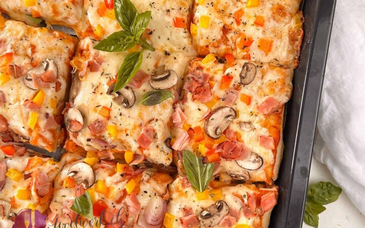 Fertig gebackene Blechpizza die geschnitten ist und noch auf dem Blech ist. Belegt mit Mozzarella, Peperoni, Pilzen und Schinken